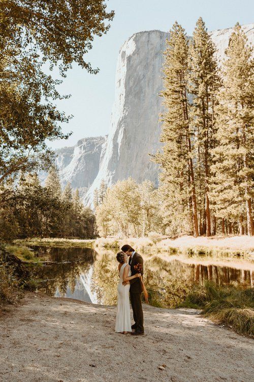 a bride and groom standing in front of a mountain lake surrounded by tall pine trees