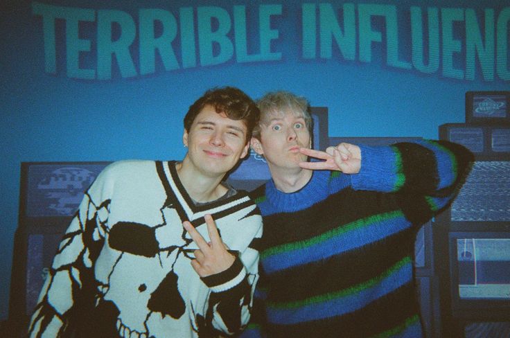 two young men standing next to each other in front of a blue wall with the words terrible