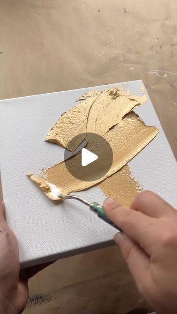 someone is painting gold leaves on a canvas with a paintbrush and some white acrylic