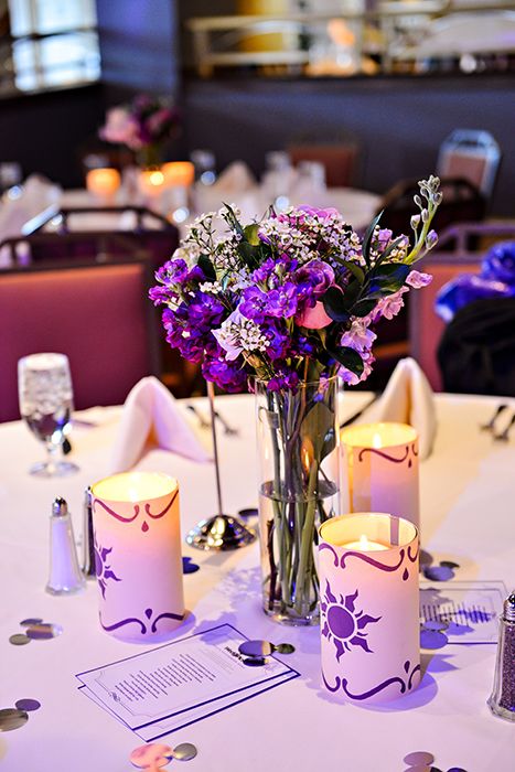 a table with purple flowers and candles on it in a fancy setting at a restaurant