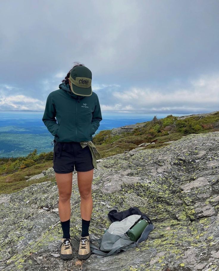 a woman standing on top of a mountain next to a backpack