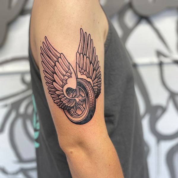 a man with a tattoo on his arm has a wheel and wings design on it