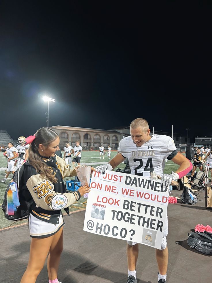 two cheerleaders holding up a sign in front of a football field at night