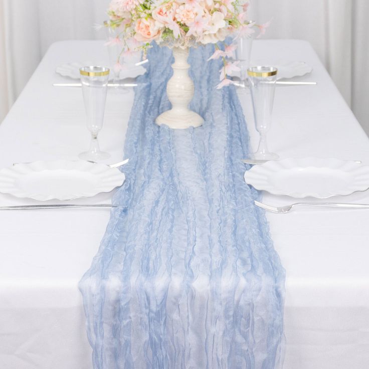 a white table topped with a vase filled with flowers next to two glasses and plates