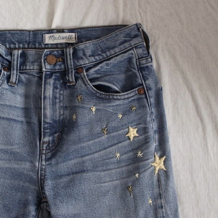 a pair of blue jeans with gold stars on the bottom and side, sitting on top of a white sheet