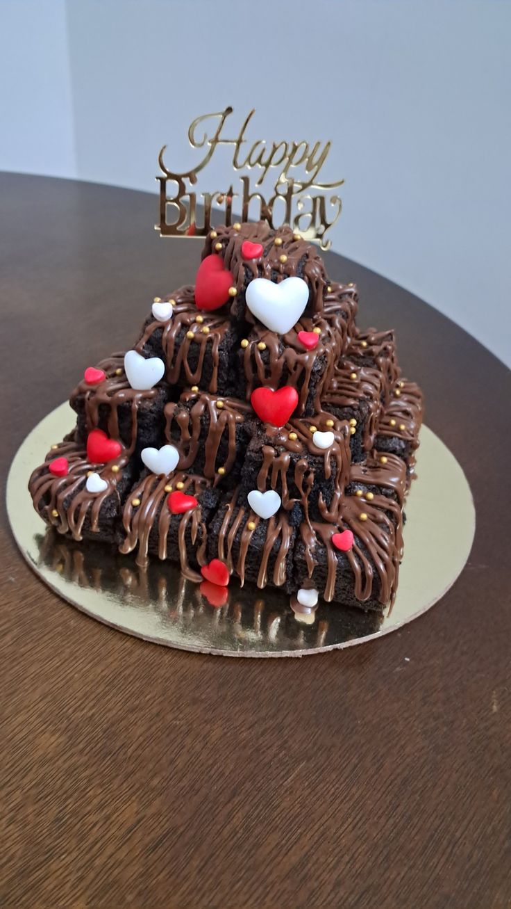 a chocolate cake with hearts on it sitting on top of a wooden table next to a happy birthday sign