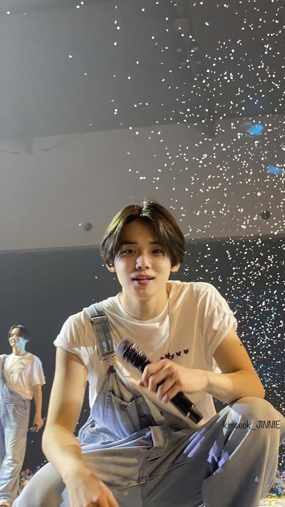 a young man sitting on the ground with a microphone in his hand and confetti falling from the ceiling