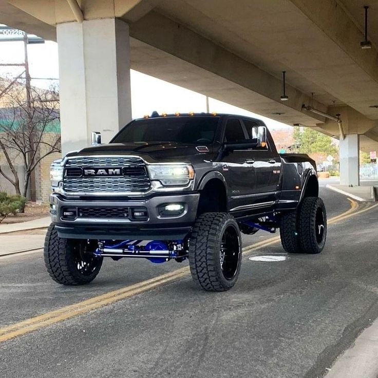 a large black truck driving down a street under an overpass in front of a building