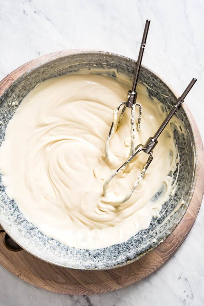 a bowl filled with cream sitting on top of a wooden cutting board next to an electric whisk