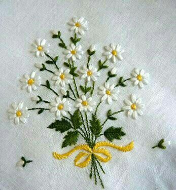 a bouquet of daisies on a white cloth with yellow ribbon and green leaves in the center