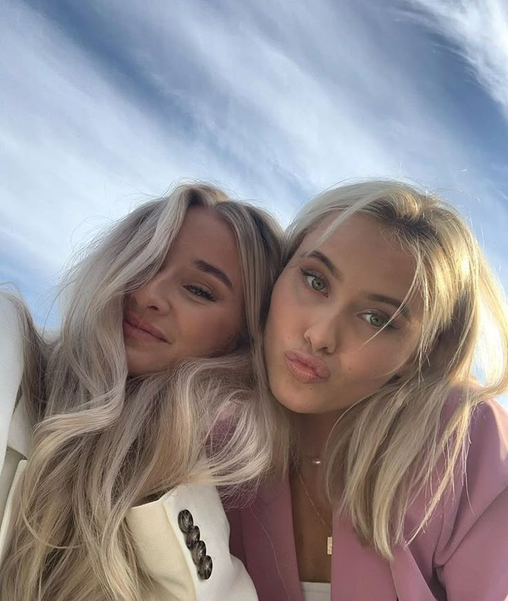 two beautiful young women sitting next to each other in front of a blue cloudy sky