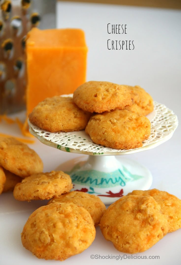 some cookies are on a white plate with orange juice and cheese in the back ground