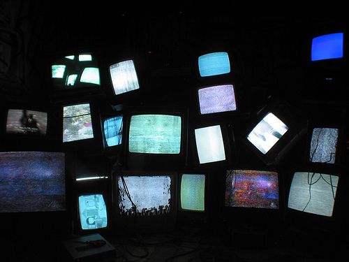 many televisions are lit up in the dark with different colors and shapes on them