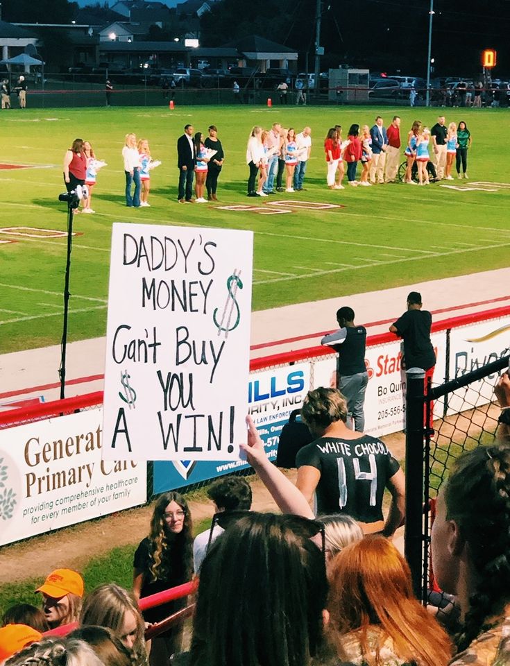 a group of people standing on top of a soccer field holding signs that read daddy's money can't buy you $ 2, get a win