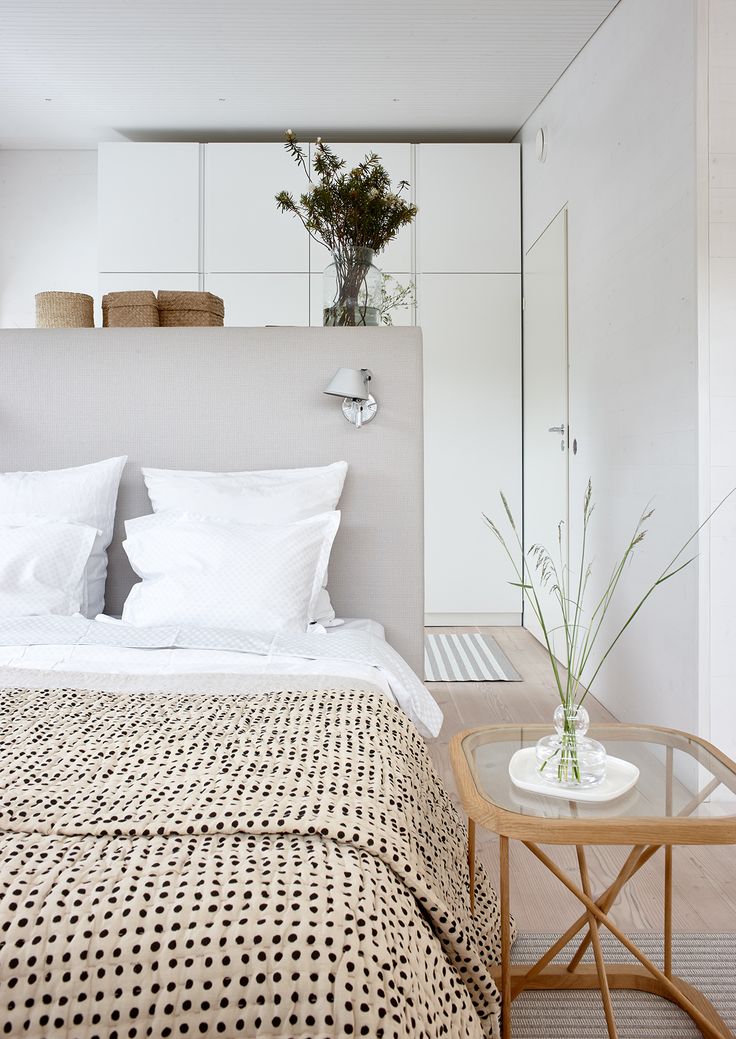 a bed with white sheets and pillows next to a small table on top of a hard wood floor