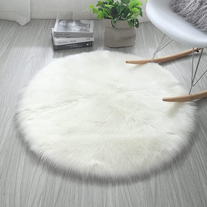 a white round rug sitting on top of a wooden floor next to a chair and potted plant