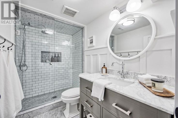 a bathroom with white tile and gray vanity, mirror, toilet, shower stall and sink