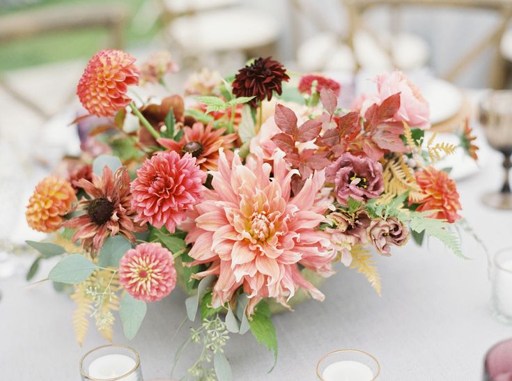 an arrangement of flowers on a table at a wedding reception with candles and napkins