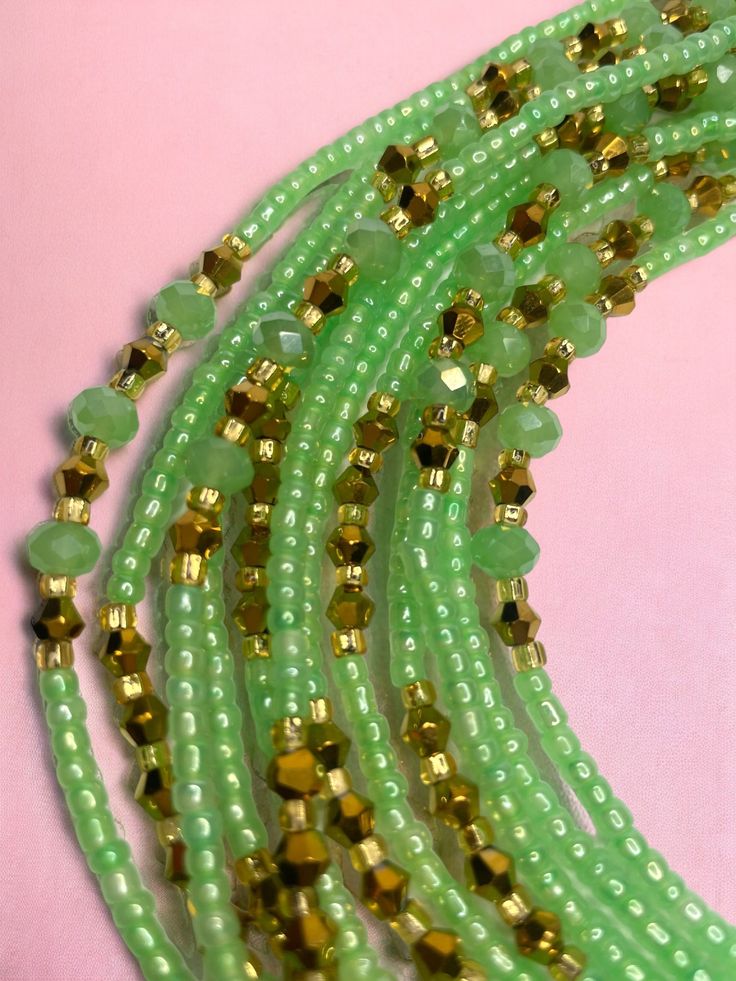 green glass beads with gold accents on a pink background, lined up in three rows