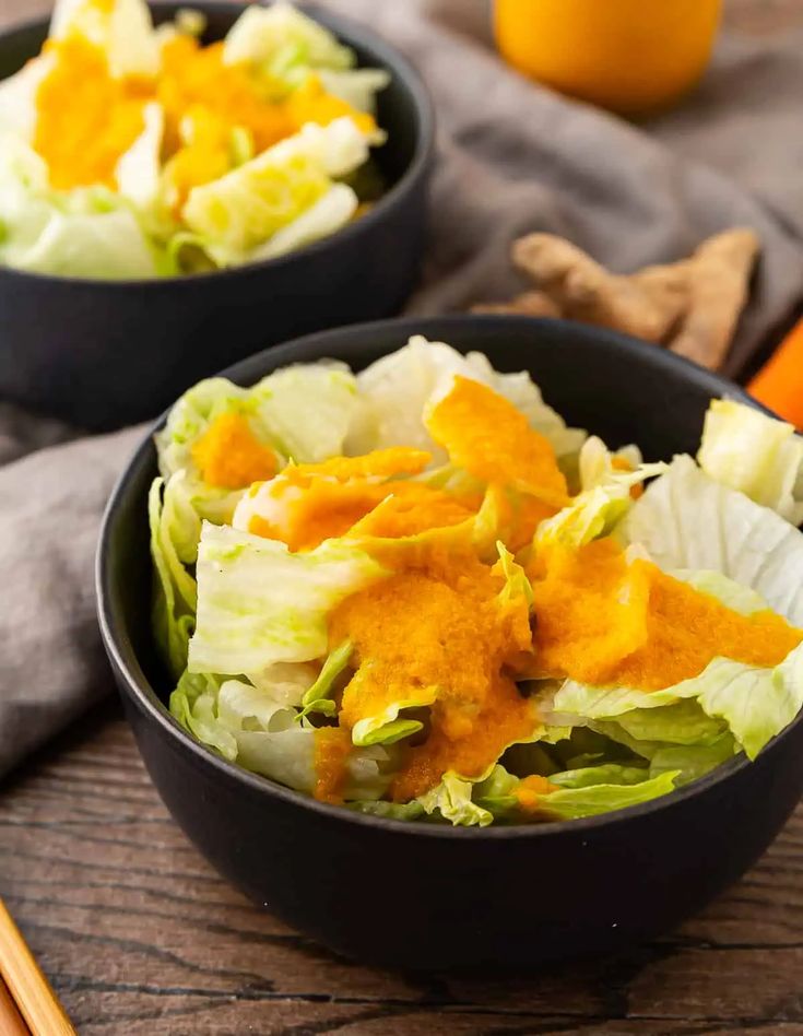 two black bowls filled with lettuce and carrots on top of a wooden table