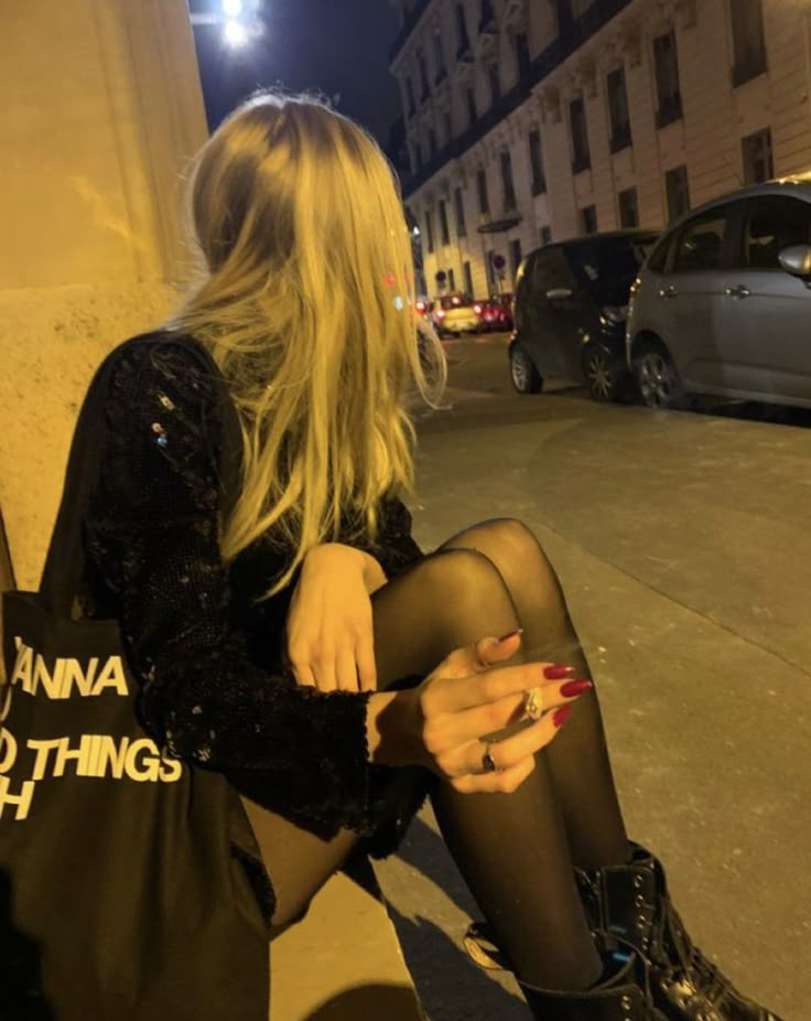 a woman sitting on the curb with her cell phone in her hand and wearing black tights