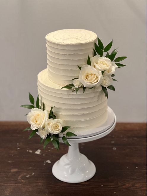 a three tiered cake with white roses on top and greenery around the edges