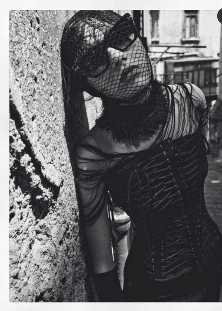 black and white photograph of a woman leaning against a wall with her face covered by netting