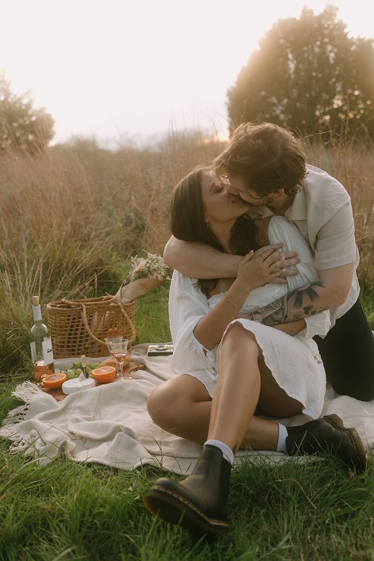 a man and woman sitting on top of a grass covered field next to each other