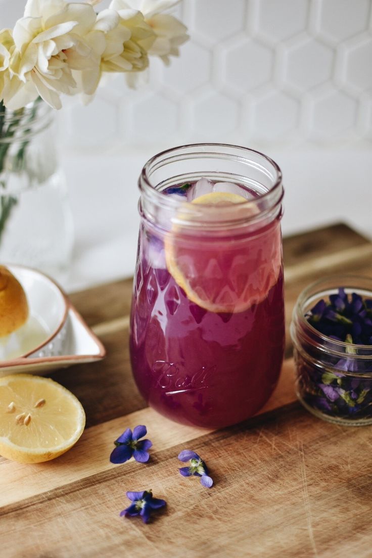 a glass jar filled with purple liquid next to sliced lemons and flowers