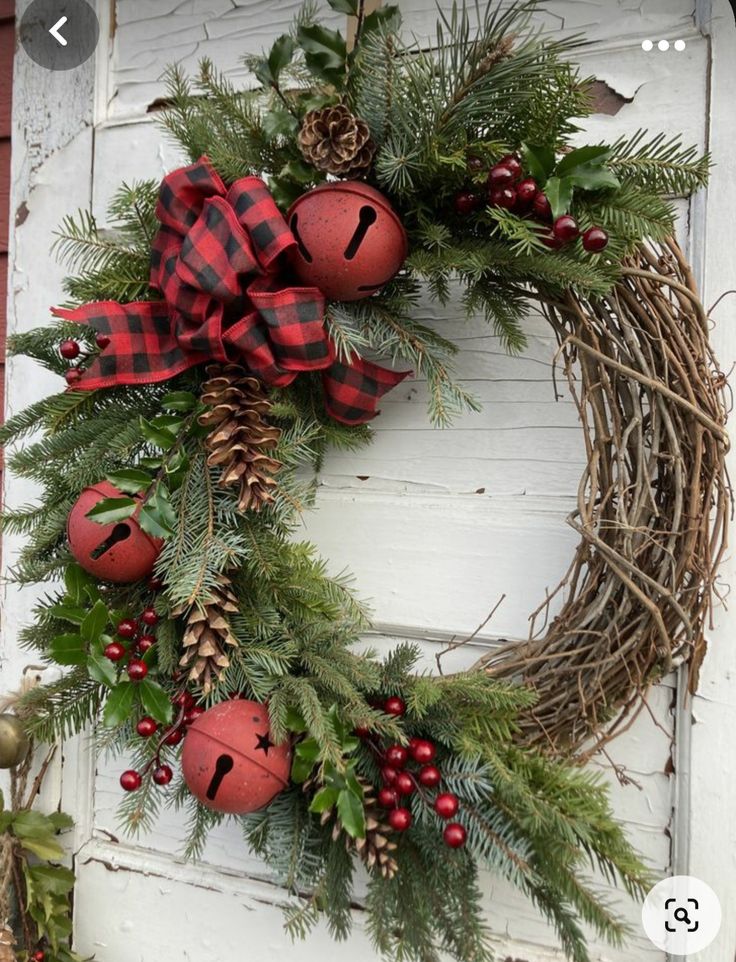 a christmas wreath hanging on the side of a door with red balls and pine cones