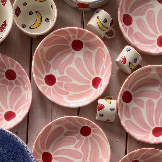 pink and white bowls with fruit painted on them sitting on a wooden table next to other dishes