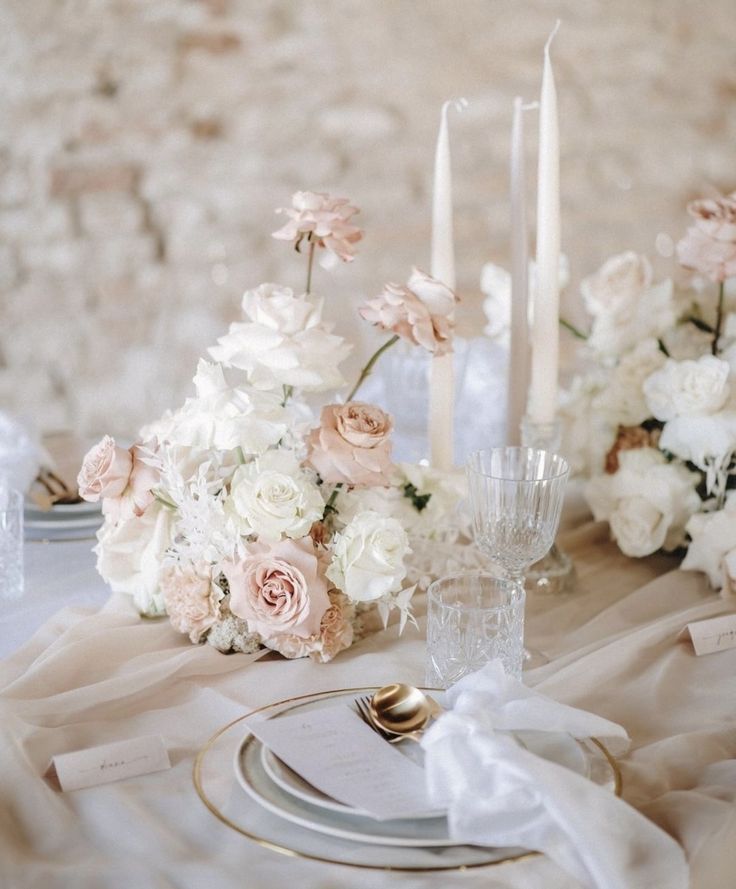 the table is set with white and pink flowers, silverware, candles and napkins