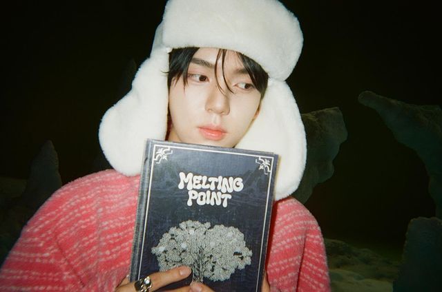 a person holding up a book in front of their face while wearing a furry hat