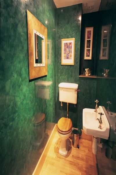 a bathroom with green walls and wood flooring is pictured in this image, there are two sinks and a toilet