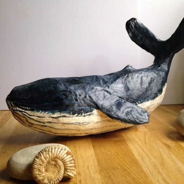 a sculpture of a whale laying on top of a wooden floor next to two sea shells