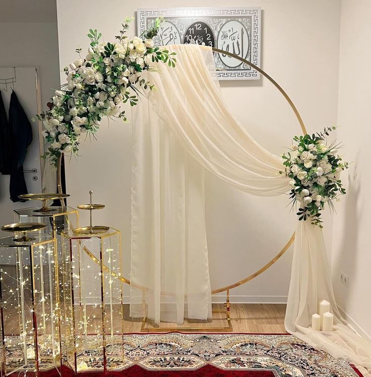 a wedding arch decorated with white flowers and greenery in front of a red rug