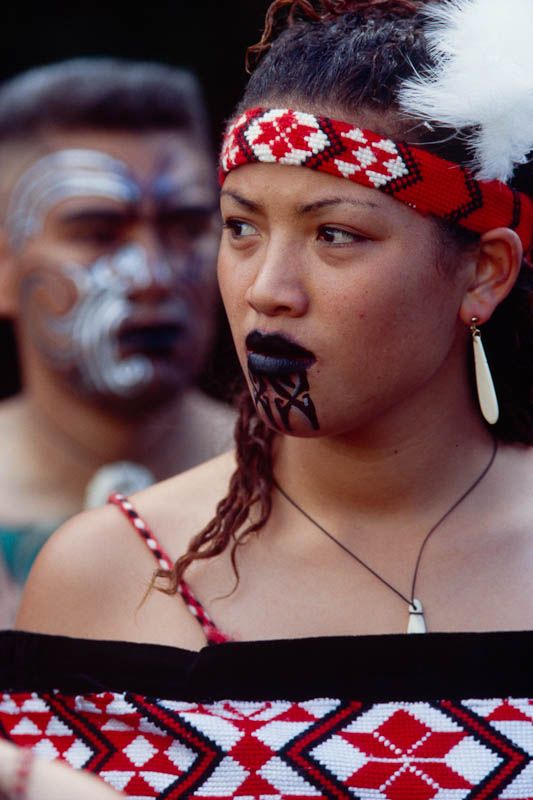 a woman with painted face and headdress standing in front of other people wearing masks