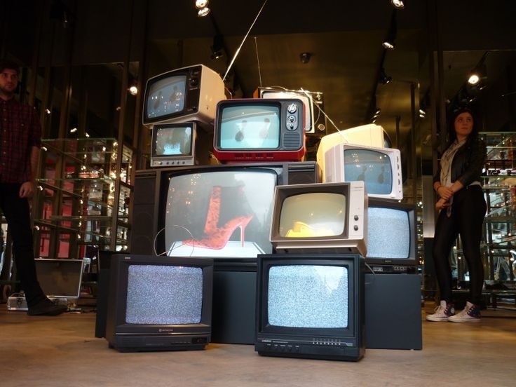 several televisions stacked on top of each other in a room with people standing around