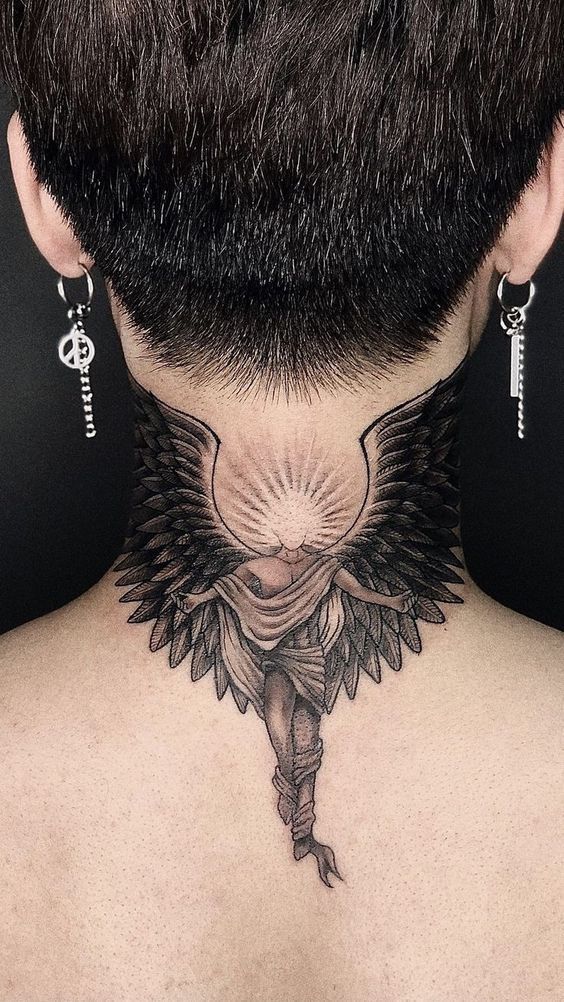 the back of a man's neck has an angel tattoo on it, and he is wearing earrings