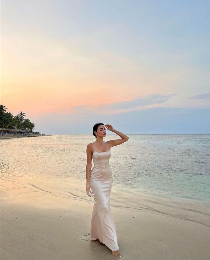 a woman standing on top of a sandy beach next to the ocean in front of an island