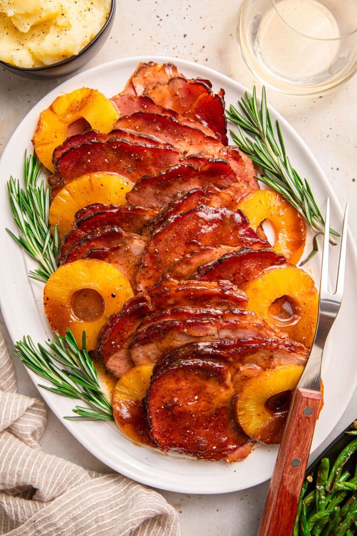 a white plate topped with bacon and pineapples next to potatoes on a table