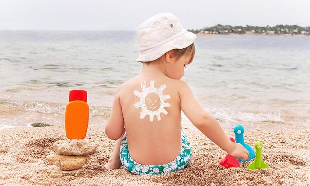 a young child sitting on the beach with sunscreen