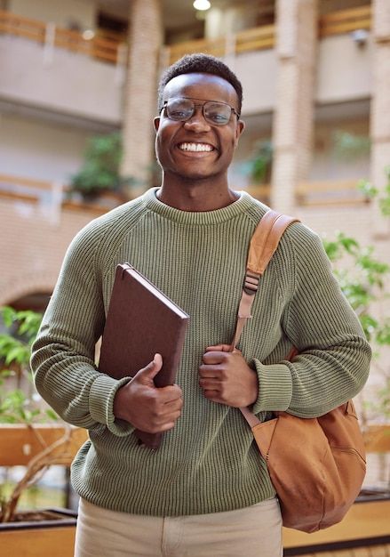 a man with glasses holding a book and smiling at the camera while standing in front of a building