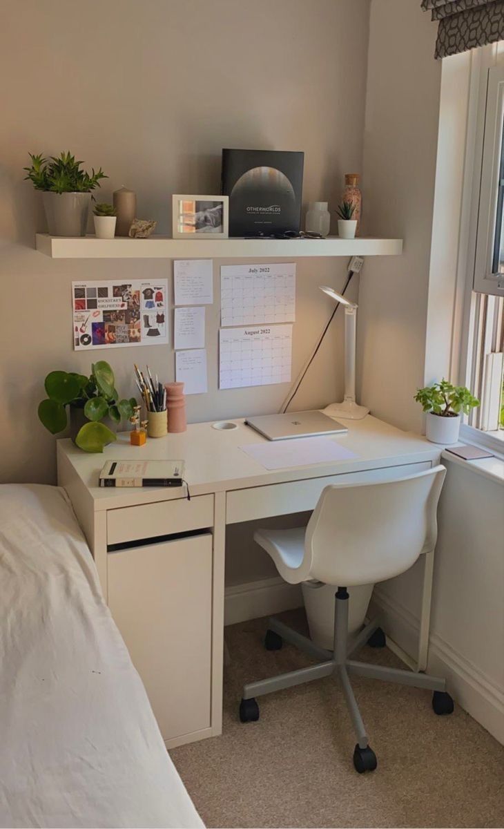 a white desk sitting in front of a window next to a lamp and potted plants