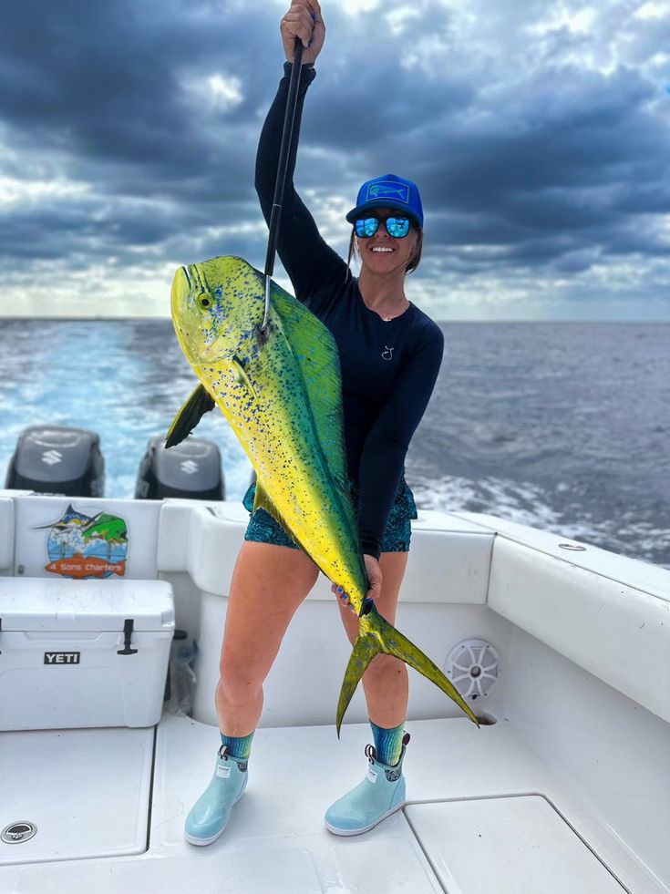 a woman holding a large fish while standing on the back of a boat in the ocean