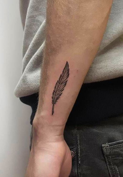 a man's arm with a small feather tattoo on it