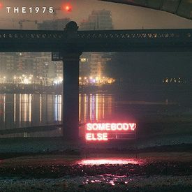 there is a neon sign that says somebody else on the side of the street under an overpass