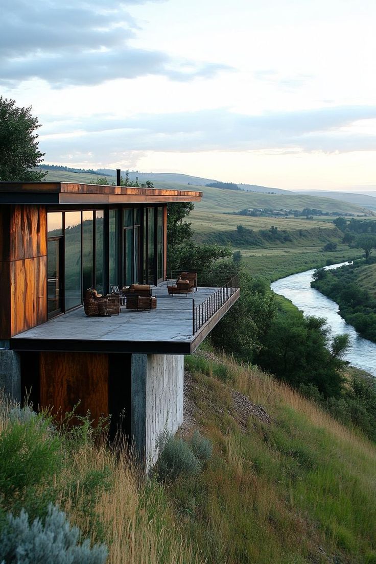 a house sitting on top of a lush green hillside next to a river in the distance