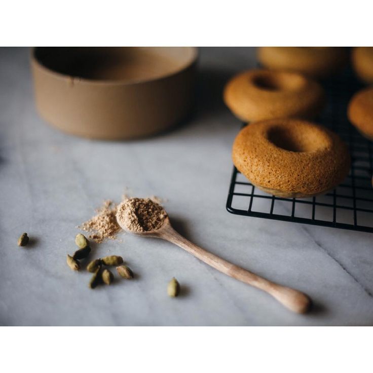 a wooden spoon filled with powder next to doughnuts on a cooling rack and other ingredients