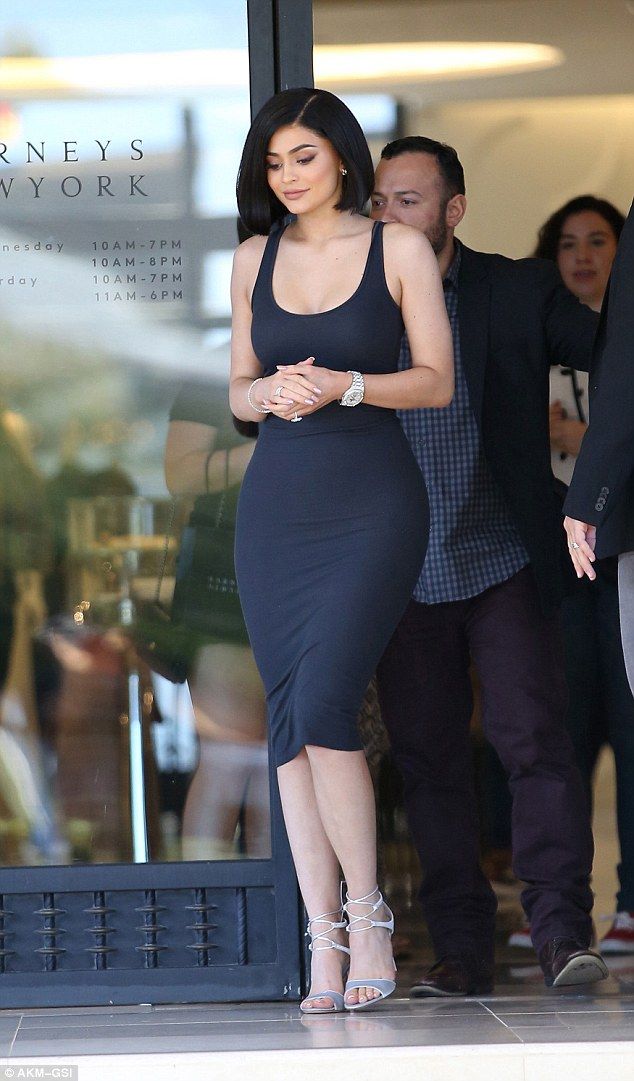 a woman in a black dress is walking out of a building with her hand on her hip